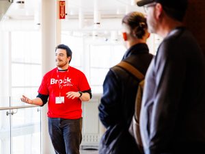 A person in a Brock University t-shirt leads a campus tour.