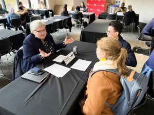 University students speak with a faculty member at a table during an international fair.