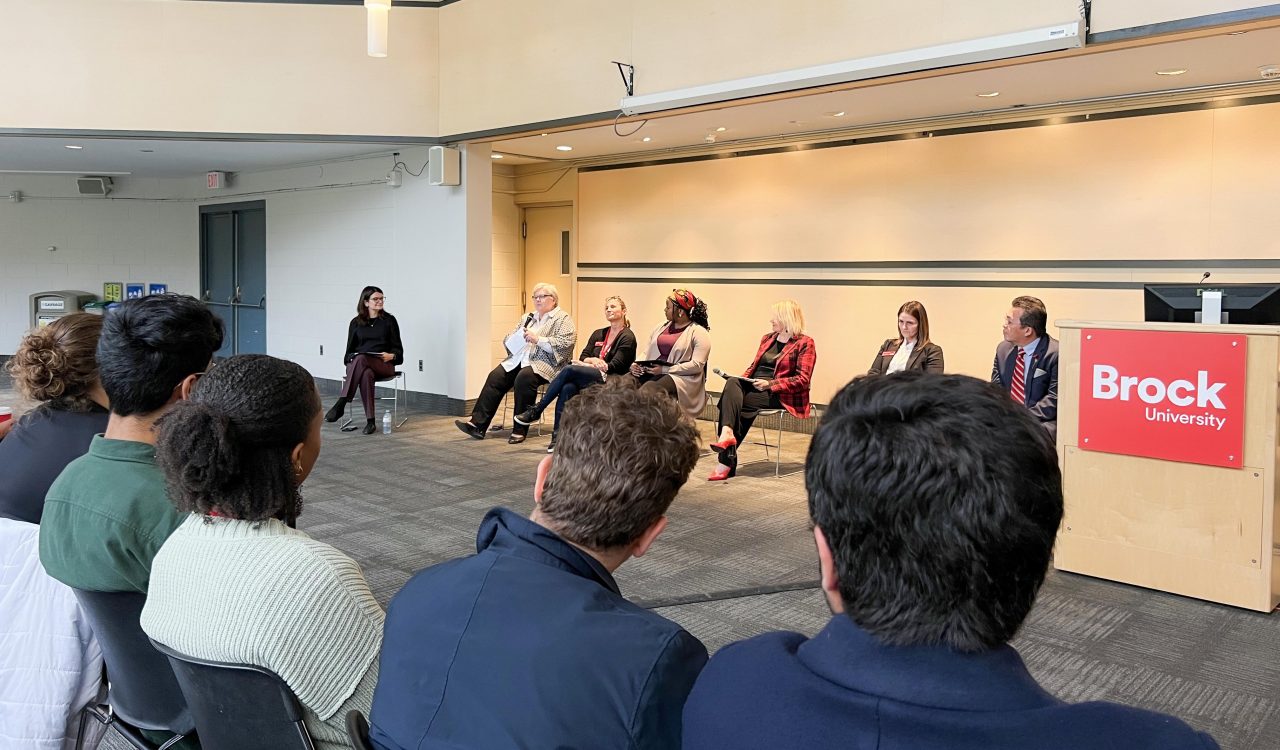 A row of speakers sits at the front of a room during a panel discussion.