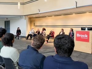 A row of speakers sits at the front of a room during a panel discussion.