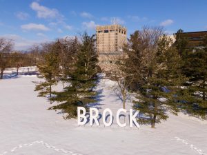 Giant letters spelling "Brock" stand in a snowy field in front of trees and a concrete tower.