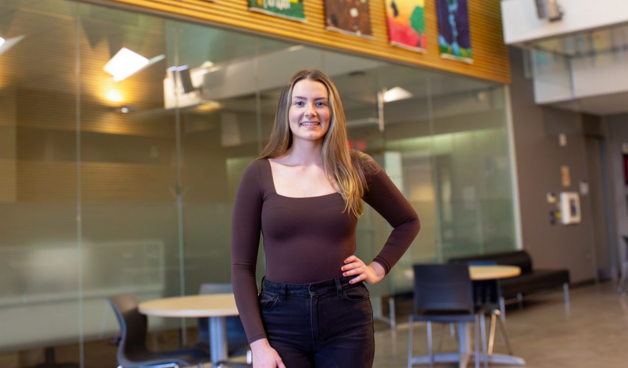 A young woman poses for a photo in a sunny atrium.