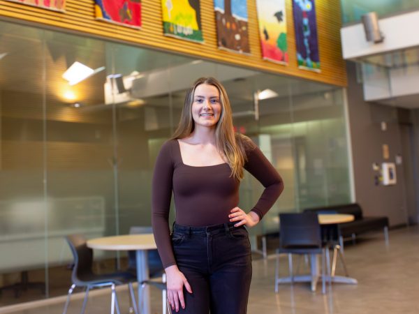 A young woman poses for a photo in a sunny atrium.