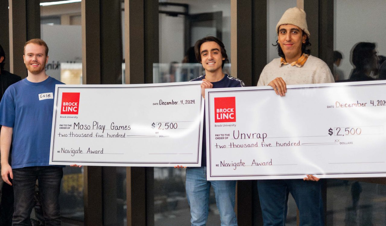 Three men pose for a photo while holding two giant cheques.