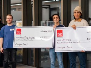 Three men pose for a photo while holding two giant cheques.