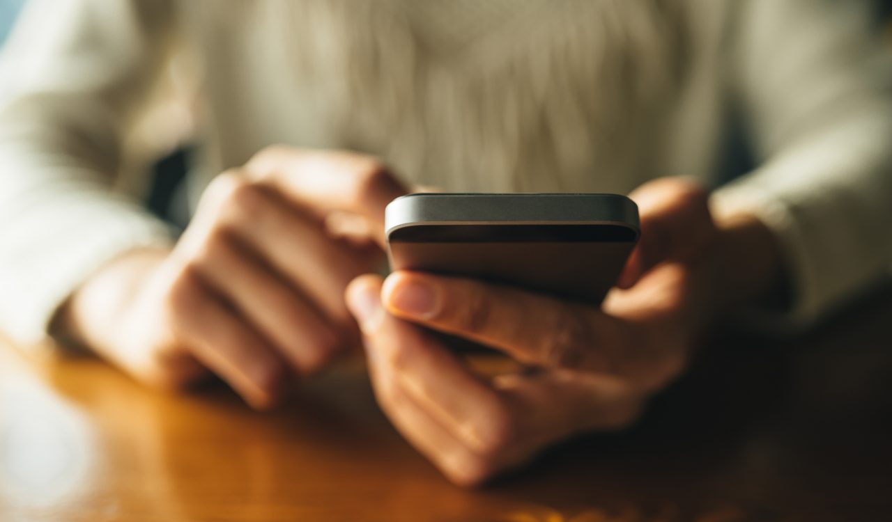 Close-up view of hands holding a smartphone over a wooden table.