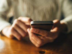 Close-up view of hands holding a smartphone over a wooden table.