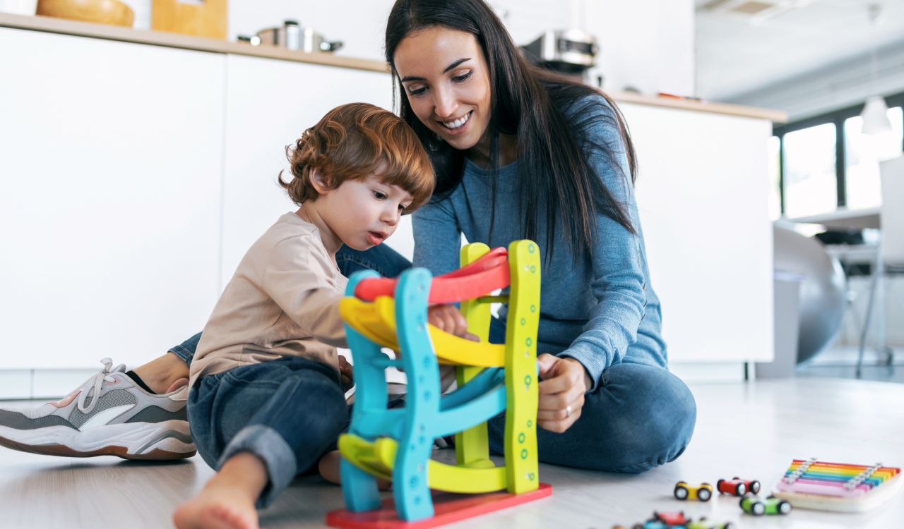 A mother and her toddler play with a toy on the floor of sunny kitchen.