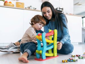 A mother and her toddler play with a toy on the floor of sunny kitchen.