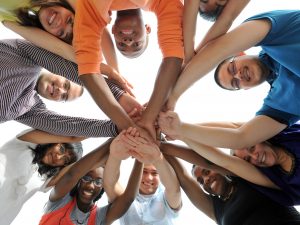 A worm’s-eye view of a group of teens putting their hands together in the middle of a circle.