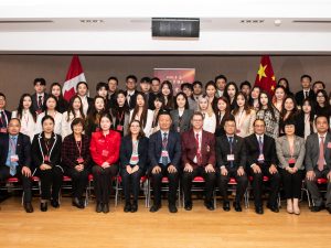 A large group of people pose for a photo in front of the Chinese and Canadian flags.