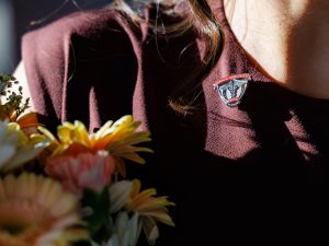 A close-up of a nursing student's maroon uniform adorned with a Brock University Nursing pin, symbolizing achievement and dedication. The student holds a bouquet of colorful flowers, emphasizing the celebratory atmosphere.