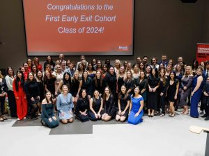 A large group of students, staff and faculty posed for a photo with a large red sign on the screen behind them reading ‘Congratulations to the First Early Exit Cohort Class of 2024!’ at Brock University on Friday, Dec. 13.