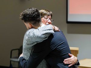 A woman delivers a congratulatory hug to a man in a black suit while standing in theatre at Brock University on Friday, Dec. 13.