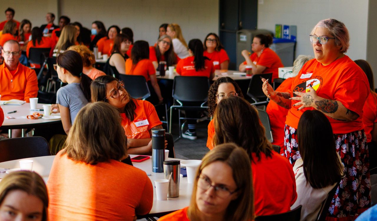 A woman wearing an orange shirt stands speaking to a large, seated group of people who are also wearing orange shirts to recognize the National Day of Truth and Reconciliation at Brock University’s Pond Inlet.