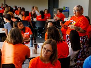 A woman wearing an orange shirt stands speaking to a large, seated group of people who are also wearing orange shirts to recognize the National Day of Truth and Reconciliation at Brock University’s Pond Inlet.