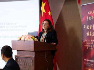 A woman presents at a podium, a large screen and Chinese flag in the background.