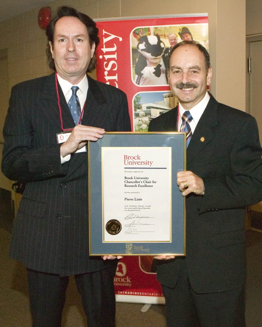 Pierre Lizée, holding a framed certificate for the Chancellor’s Chair for Research Excellence, with Jack Lightstone