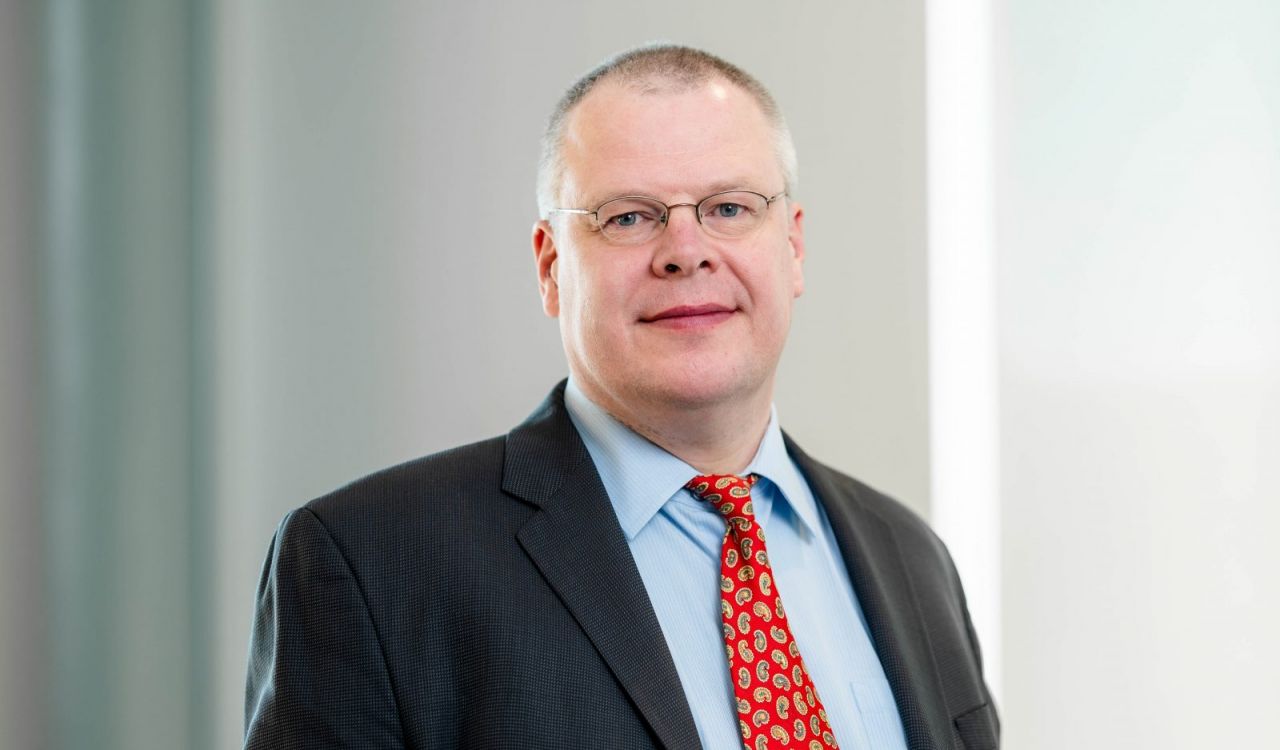 A man in a suit poses for a headshot beside a window.