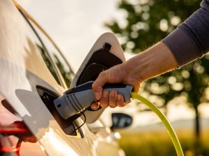 Close-up view of a hand holding an electric vehicle plug while attaching it to a car.