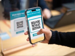 Close-up view of a hand holding a cellphone while someone scans a QR code.