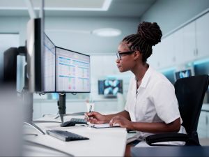 A woman sits at a desk in a health care setting working on a series of computer screens.