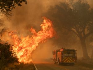 A fire truck drives on a road beside a wildfire in Valyermo in the United States.