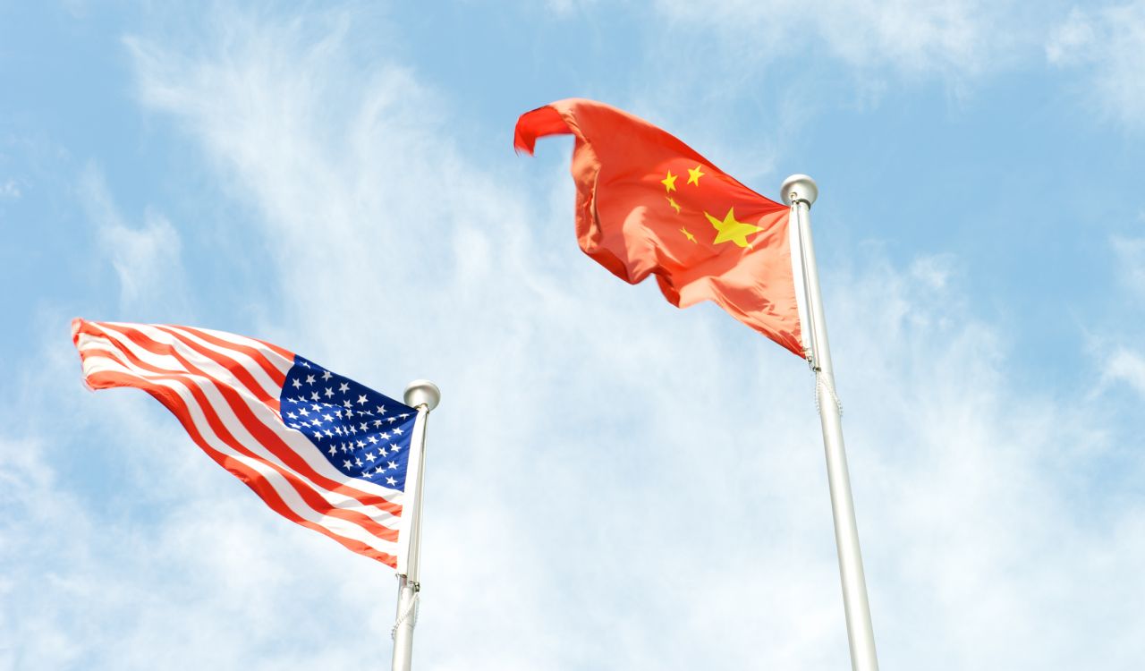 The American and Chinese flags fly beside each other against a partly cloudy sky.