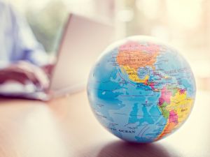 Close-up of a globe on a table with a person working on a laptop in the background.