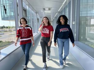 Three young women walk down a sunny hallway in a university.