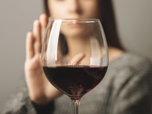 Close-up of a glass of red wine with a woman's hand held up to refuse it in the background.