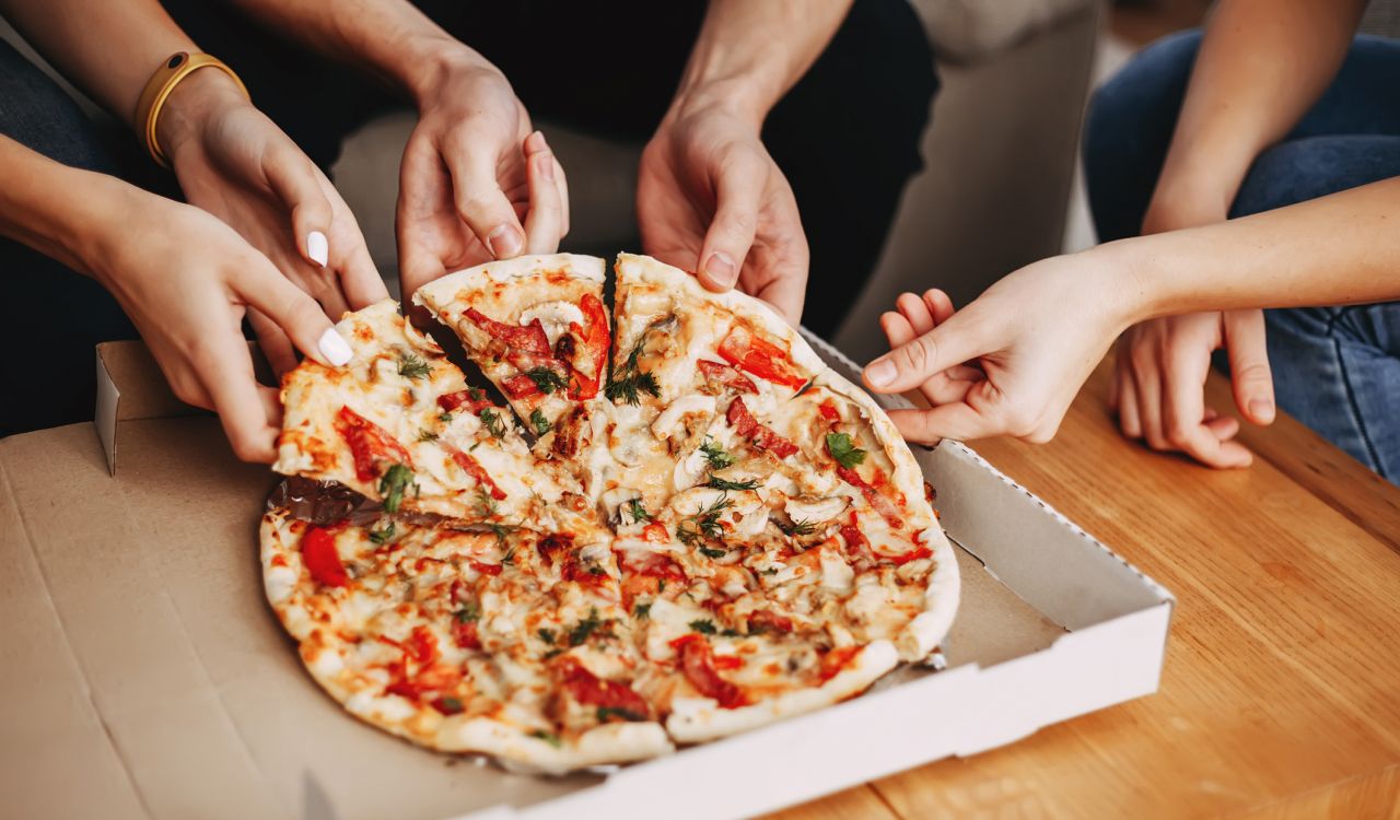 Hands of young people taking pizza slices from a box.