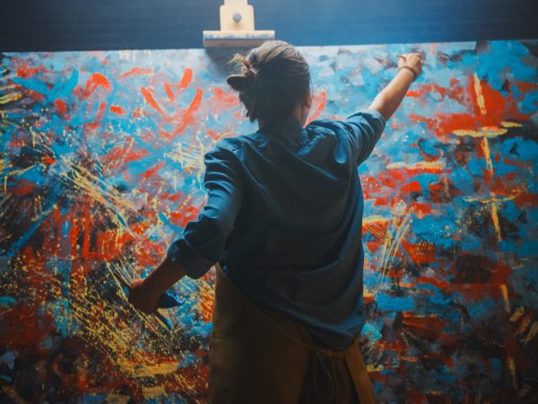 An artist, seen from behind, paints on a large canvas.
