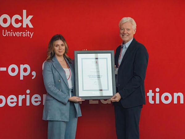 A man and a woman pose holding a framed certificate between them.