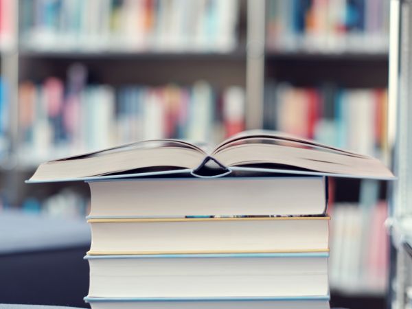 An open book sits on a stack of other books on a table in a library.