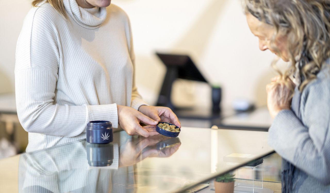 An older woman looks at cannabis products held by an employee at a retail store.