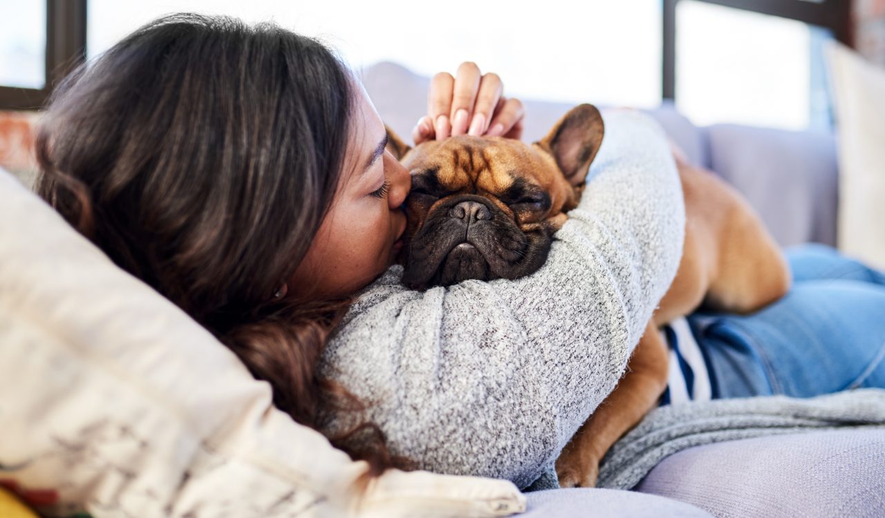 A woman snuggles her dog on a couch.