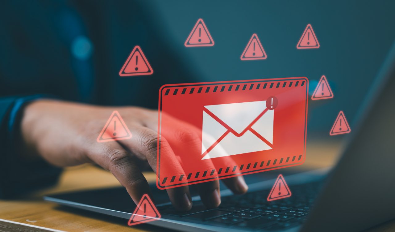 An email icon floats over a laptop keyboard surrounded by warning icons.