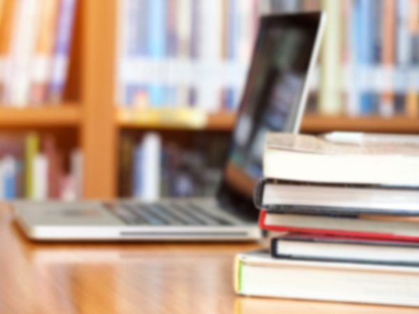 A laptop next to a pile of books in a library.