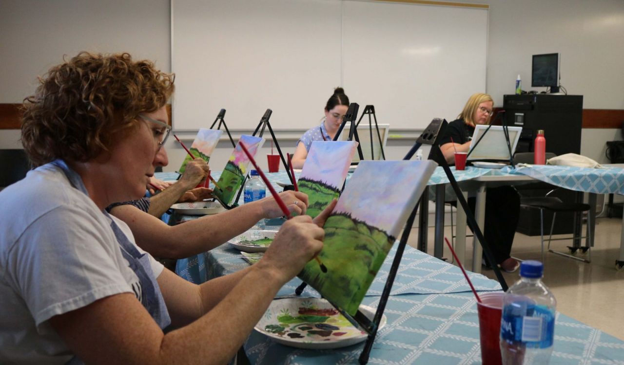People sit at tables painting landscapes.