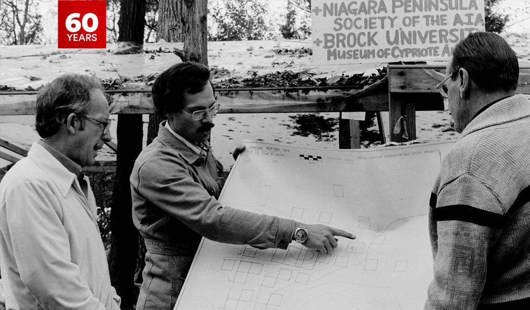 Close-up photo of three people standing in front of a map in the 1970s.