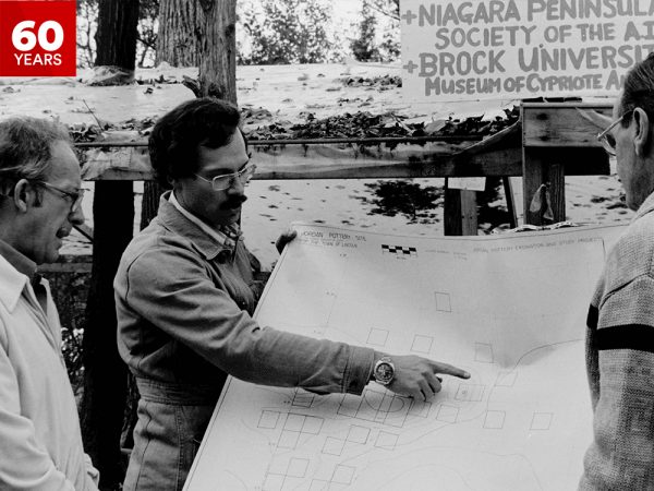 Close-up photo of three people standing in front of a map in the 1970s.