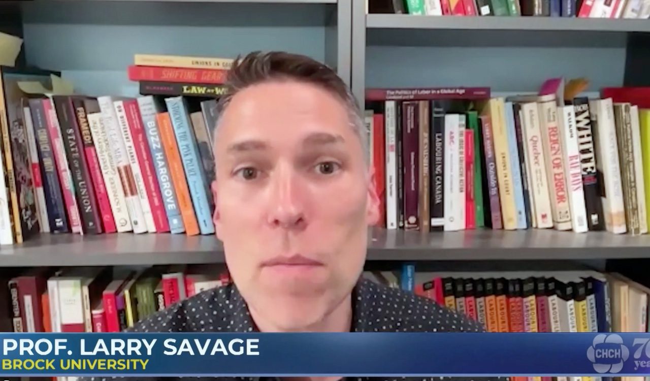 Man sits in front of bookshelf and does a television interview.