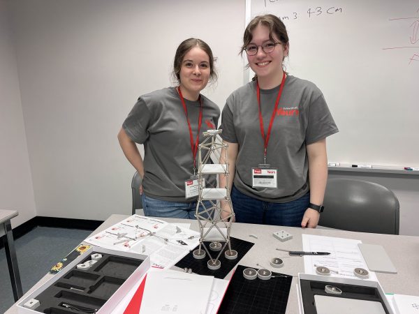 Two teenage girls pose with a structure they built during an engineering activity.
