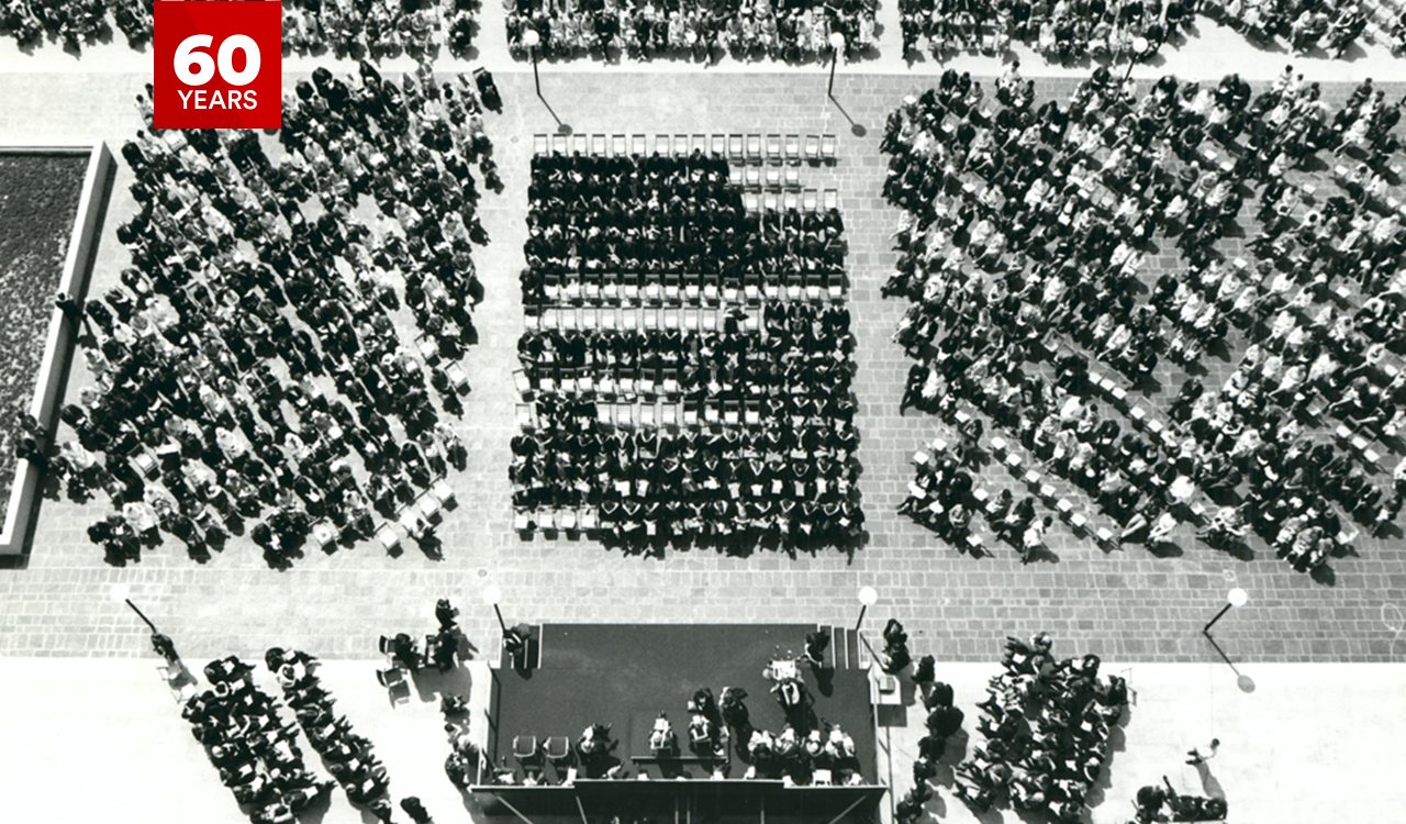 An aerial black and white photo of a university convocation with graduates and guests seated in an outdoor space pictured below.