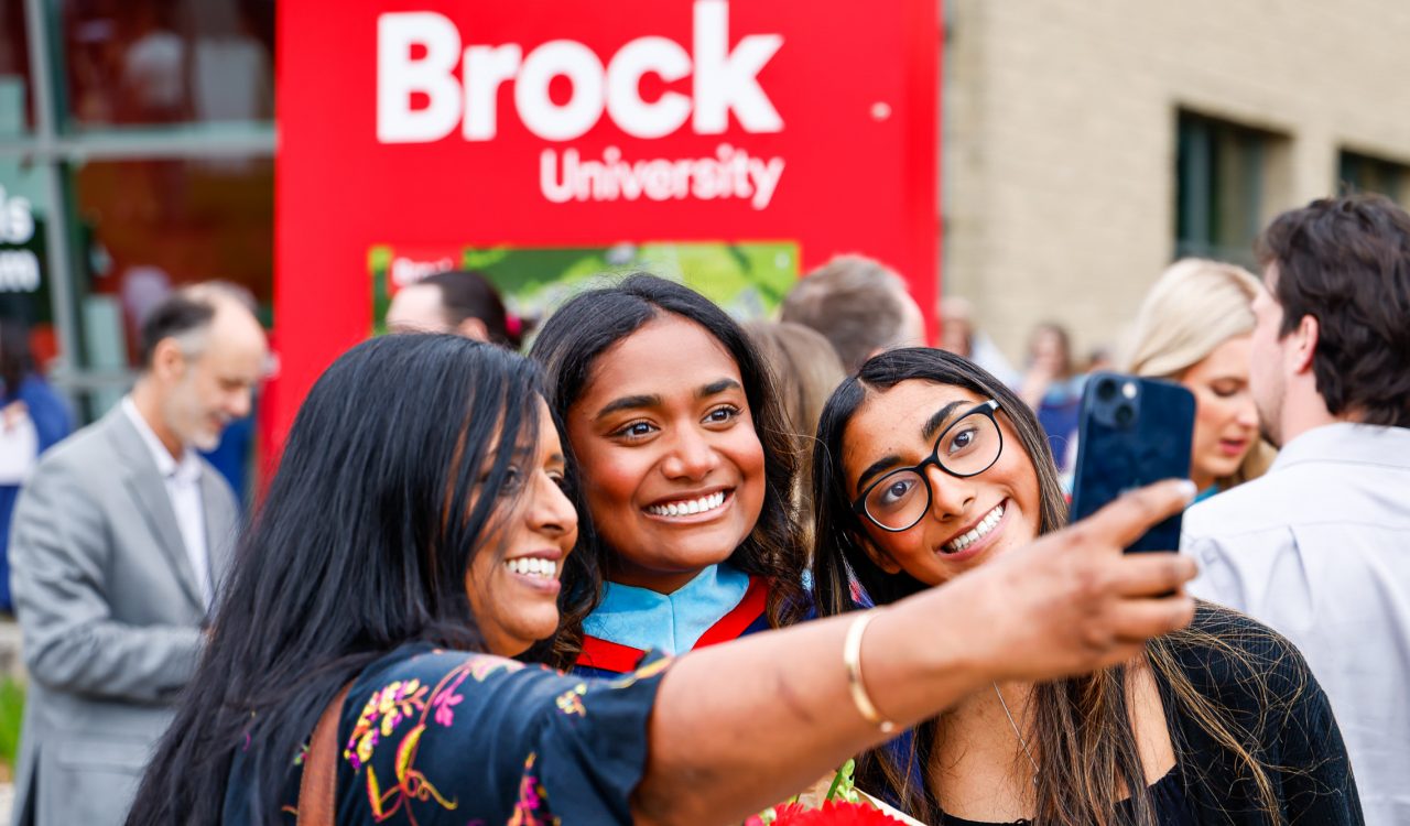 A new university graduate takes a selfie with loved ones.