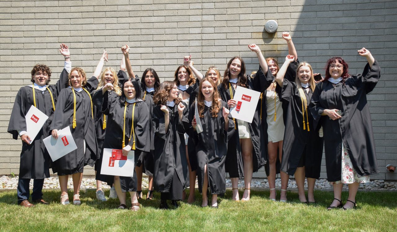 A group of students in academic robes cheer outside after a university graduation ceremony.