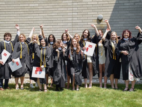 A group of students in academic robes cheer outside after a university graduation ceremony.
