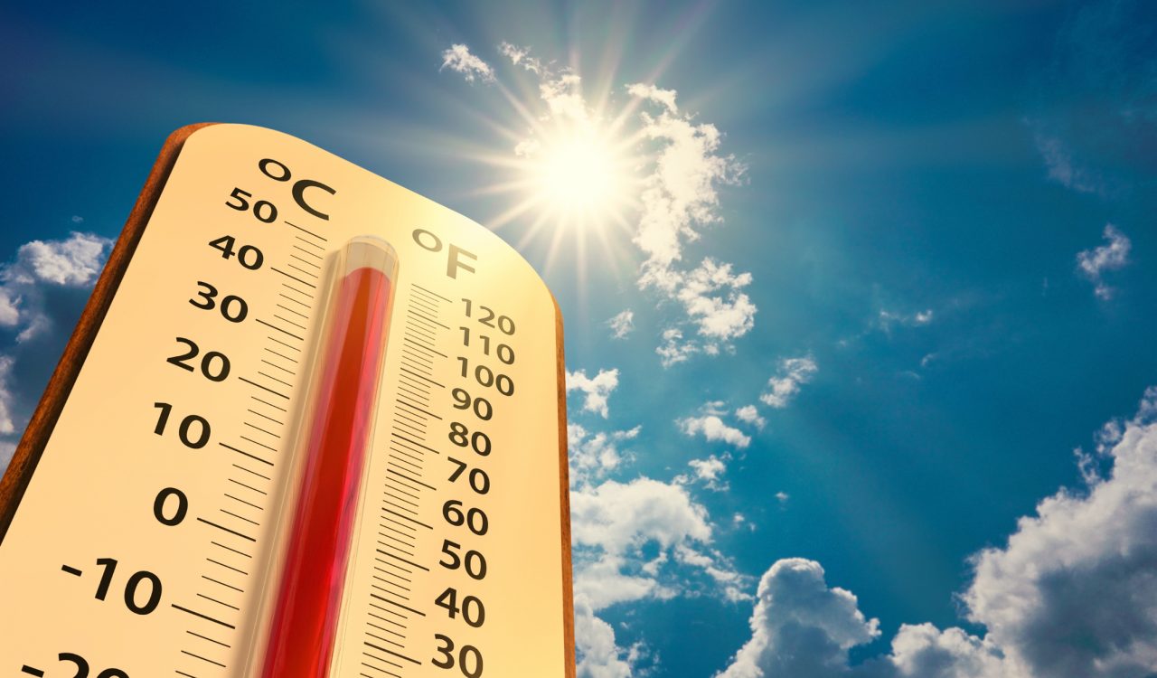 A thermometer with high heat temperatures stands beside a blue sky and sunshine.