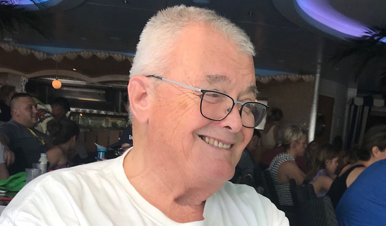 A man wearing glasses sits while smiling off camera.